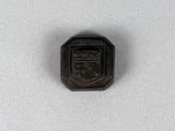 un petit objet métallique noir orné d'un blason