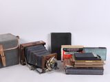 un vieil appareil photo, un livre, un étui à appareil photo et d'autres objets sont posés sur une surface blanche