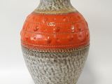 un vase orange et gris posé sur une surface blanche