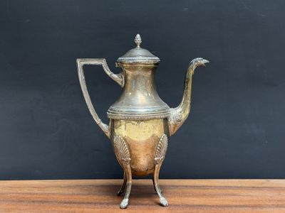 an antique silver tea pot on a wooden table against a black wall