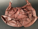brown leather handbag with pleated handles on a black surface