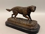 statue en bronze représentant un chien en train de courir, posée sur un socle, sur fond blanc