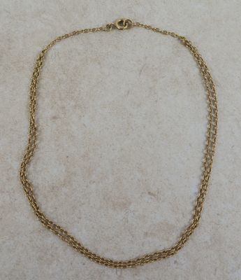 un gros plan d'un collier à chaîne en or posé sur une surface en marbre