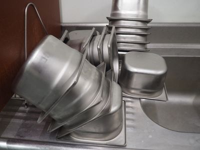 Des casseroles et poêles en argent sont empilées dans un évier équipé d'un égouttoir.