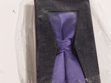 une cravate violette dans une boîte noire posée sur une surface blanche