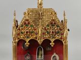 une horloge dorée et rouge posée sur un socle, sur une surface blanche