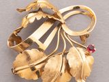 an image of a gold broochle with leaves and a red stone