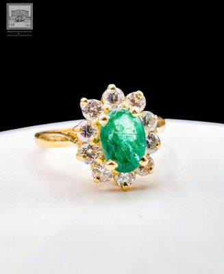 a close up of a green emerald and diamond ring on a white plate