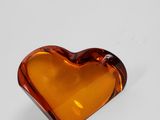 an orange glass heart shaped object sitting on top of a white surface