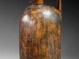 an old brown jug with a wooden handle sitting on a table