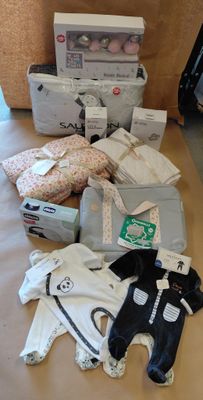 une pile de vêtements de bébé posée sur une table à côté d'une valise