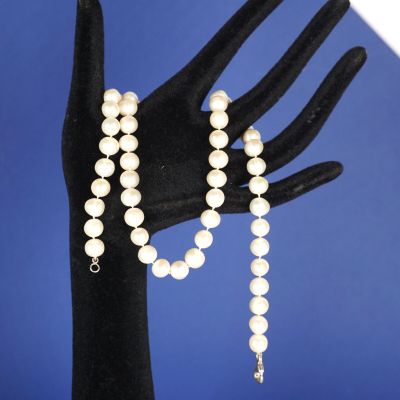 la main d'une femme tenant un collier et un bracelet de perles blanches