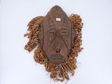 an old wooden mask with fringes on a white surface
