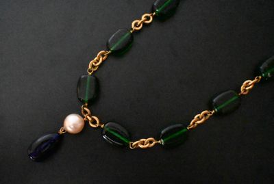 a close up of a necklace with a pearl and green glass beads