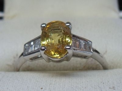 une photo d'une bague sertie d'un saphir jaune et de diamants, posée sur un tissu blanc