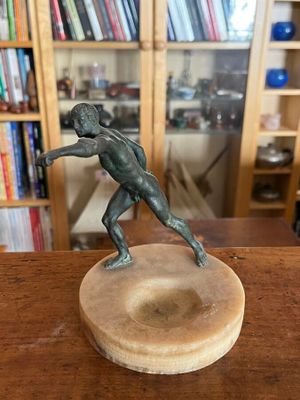 statue en bronze représentant un homme tenant une raquette de tennis, posée sur un socle en bois