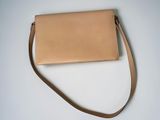 a tan leather purse with a brown strap on a white surface