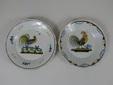 two plates with roosters painted on them sitting on a table