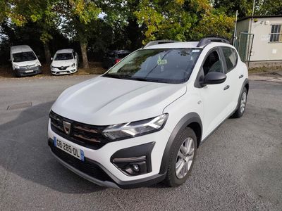 La voiture blanche est garée sur le parking, près des arbres.