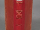 an old red book sitting on top of a table next to a gray wall