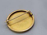 gold plated pin with a circular design on a gray surface