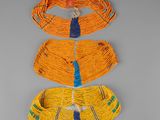 trois vêtements tissés, jaunes et bleus, accrochés à un mur