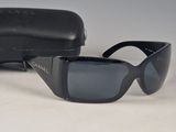 Lunettes de soleil Chanel à monture noire, avec leur étui, posées sur une surface blanche