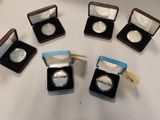 six silver coins are in small cases on a white surface