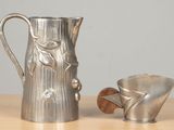 a silver pitcher and a silver cup on a table