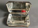 an open silver box with a red handle sitting on a table