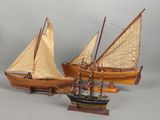 trois maquettes de bateaux en bois avec des voiles, exposées sur un fond gris