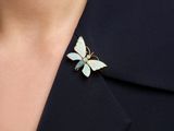 a close up of a woman wearing a gold and white butterfly broochle