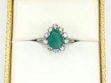 an emerald and diamond ring in a gold box on a white surface