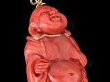 statue d'un Bouddha rouge souriant posée sur un socle plaqué or, sur fond noir
