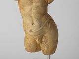 une statue antique représentant un torse masculin posée sur un socle transparent