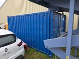 une voiture blanche garée à côté d'un conteneur d'expédition bleu