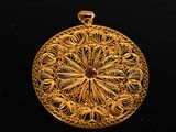 gold filigree pendant with a red stone in the center