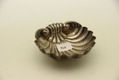 un petit objet argenté en forme de coquillage posé sur une surface blanche