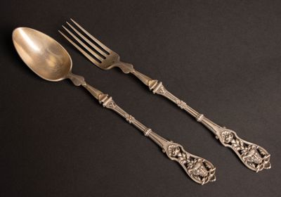 two silver spoons and a fork on a black surface