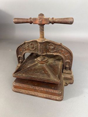 une vieille presse en fonte avec une poignée en bois posée sur une surface blanche