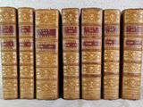 six old books are lined up on a white surface