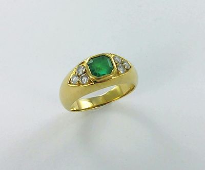 gros plan d'une bague en or avec une pierre verte et des diamants