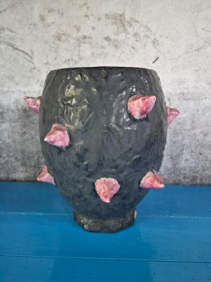 a black vase with pink flowers on it on a blue table