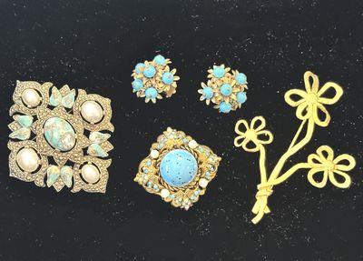 trois broches en or et turquoise et une paire de boucles d'oreilles posées sur un fond noir
