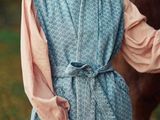 une femme vêtue d'une tenue bleue et rose, debout à côté d'un cheval dans un champ