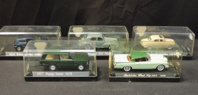 three green and white model cars in clear boxes on a black surface