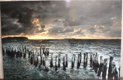 tableau représentant un coucher de soleil sur un plan d'eau, avec des poteaux en bois au premier plan