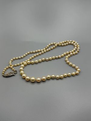 un collier de perles avec un fermoir en argent sur fond gris