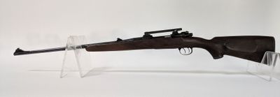 Le fusil est exposé sur un socle en acrylique transparent.