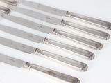 six silverplated knives are lined up in a row on a white surface
